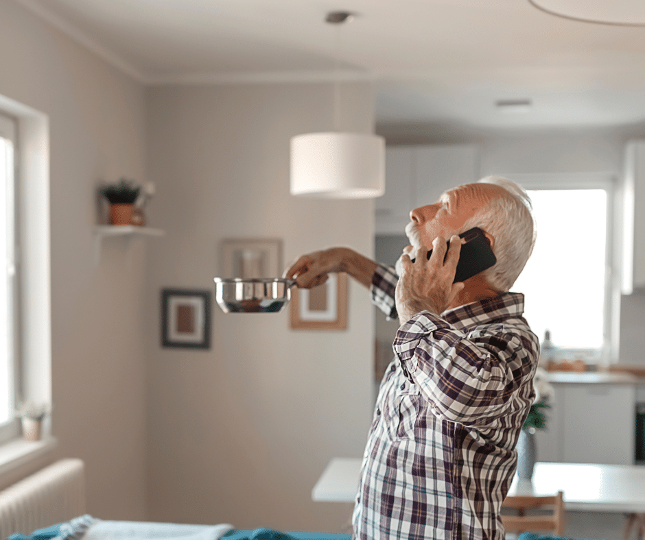 homme regardant le plafond qui fuit avec une casserole dans la main